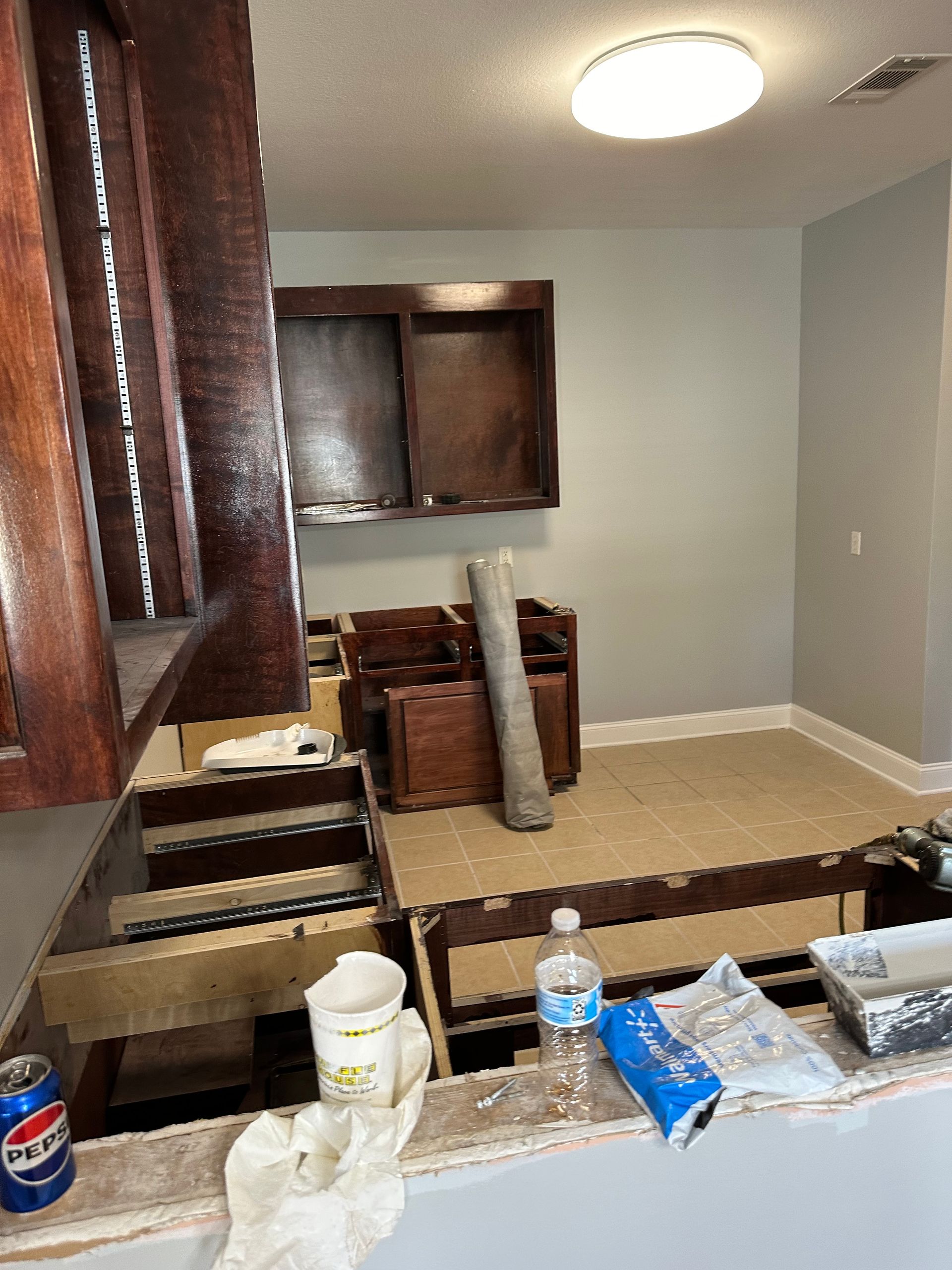 Interior during renovation; cabinetry, partially disassembled. Flooring, exposed supports. Paint, tools, debris scattered.