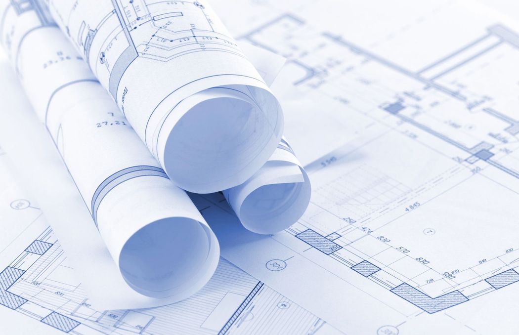 Rolled architectural blueprints on a drafting plan with faint technical drawings underneath