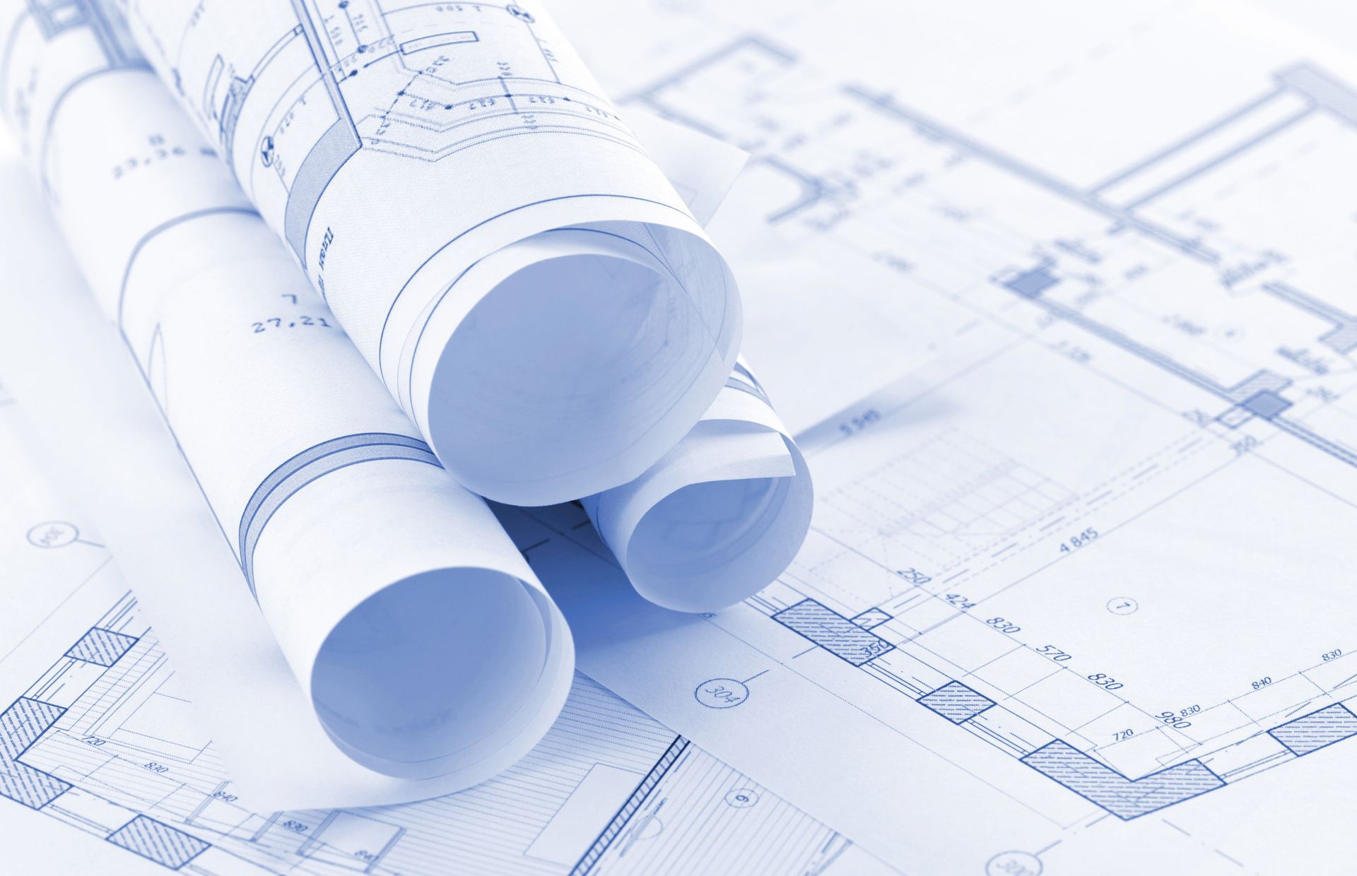 Rolled architectural blueprints on a drafting plan with faint technical drawings underneath