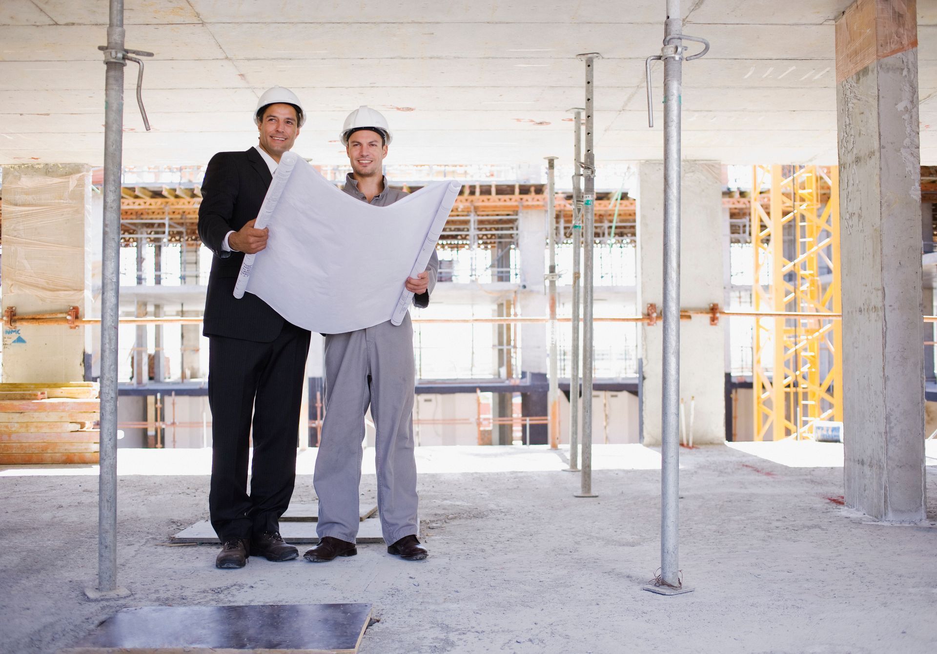 Two people reviewing blueprints inside a construction site