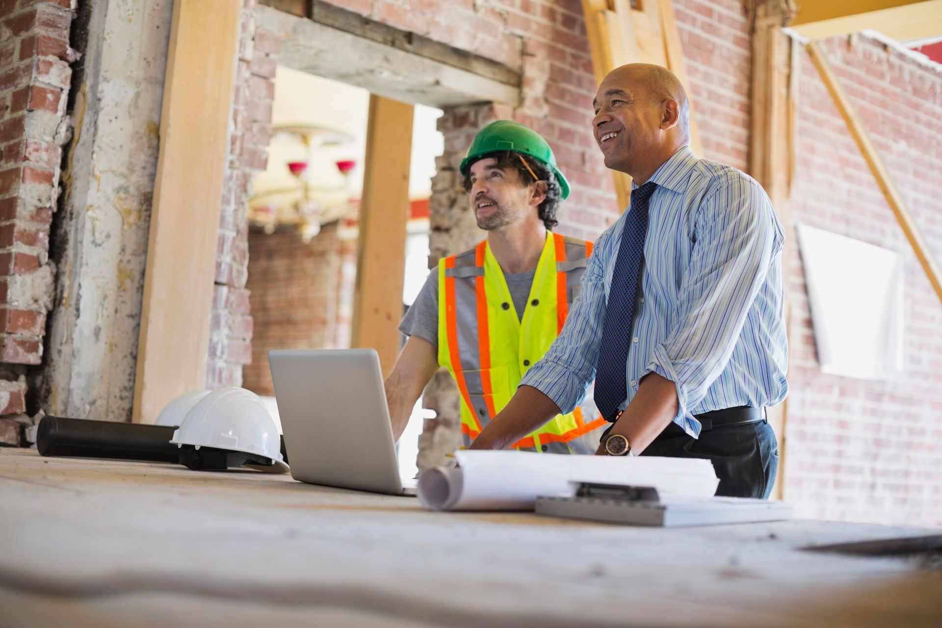 Two construction workers reviewing plans on a laptop at a building site