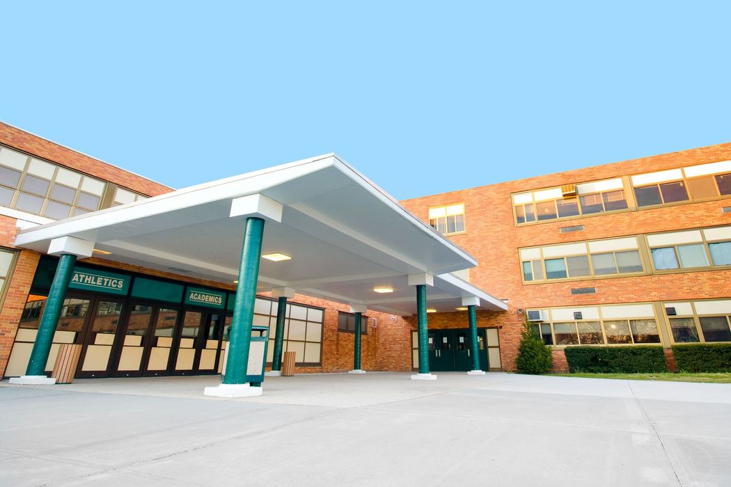 Modern brick school entrance with white canopy and glass doors under a clear blue sky