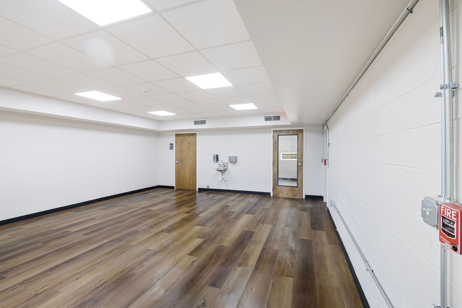 Empty office room with wood floors, white walls, and recessed ceiling lights