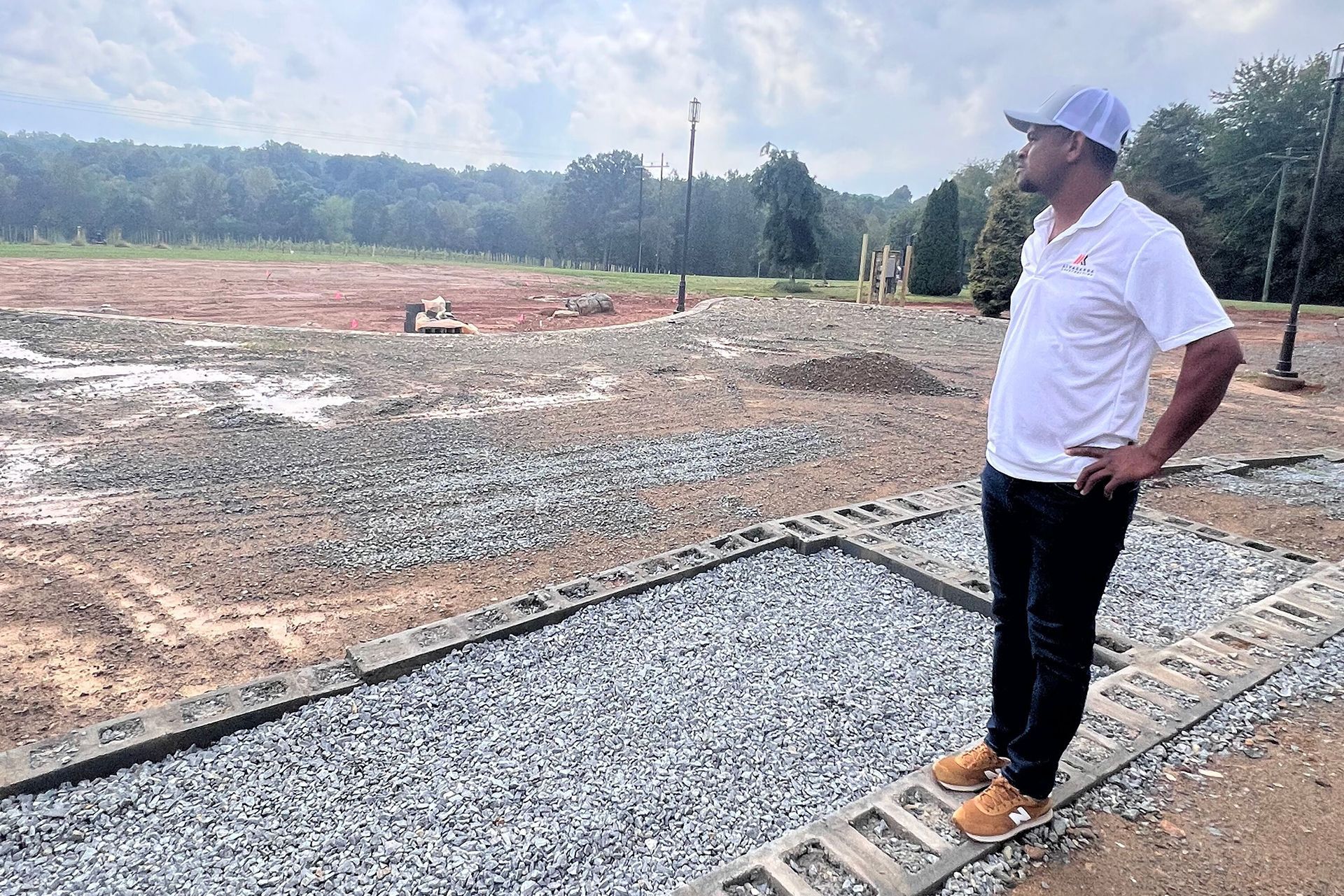 Man standing on a gravel path overlooking a cleared construction site and tree line