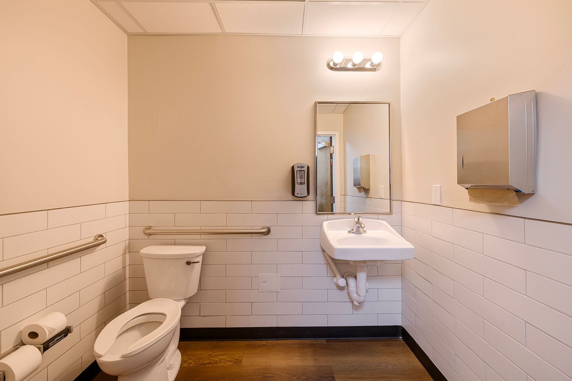 Accessible restroom with toilet, sink, mirror, grab bars, and wall-mounted dispensers