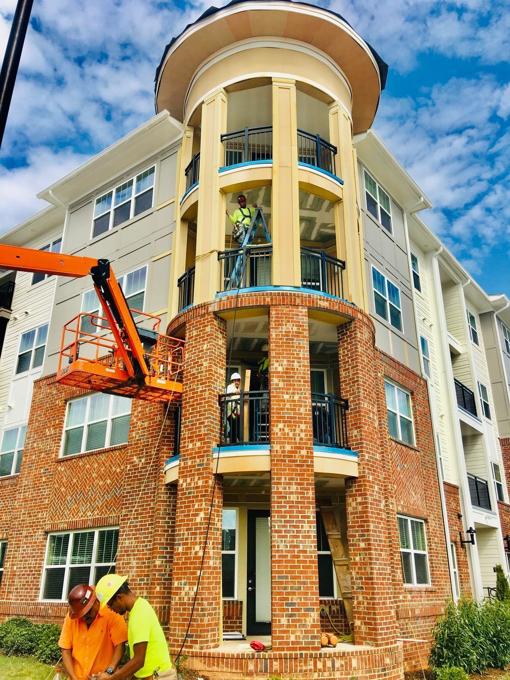 Construction worker on a lift repairing a brick apartment building corner with balconies