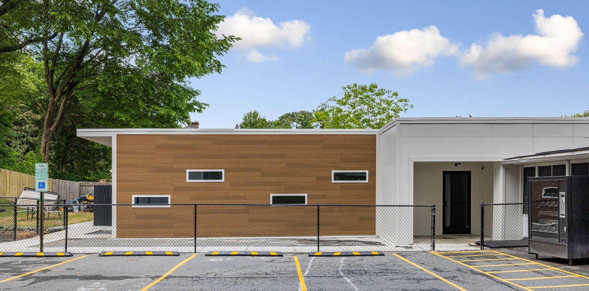 Modern brick-and-white building exterior with a parking area and trees