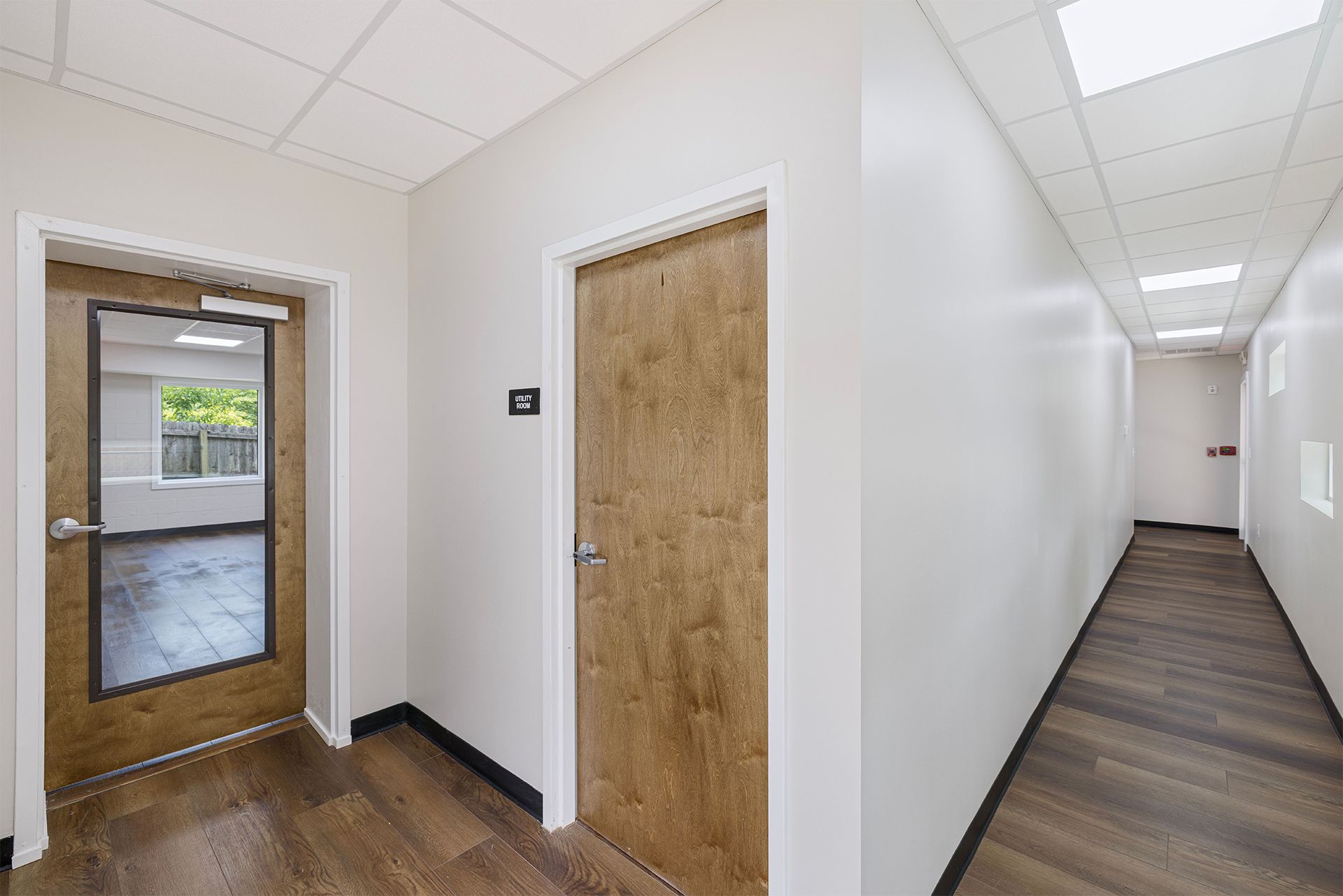 Office hallway with wood doors, white walls, and carpeted corridor under fluorescent lights.