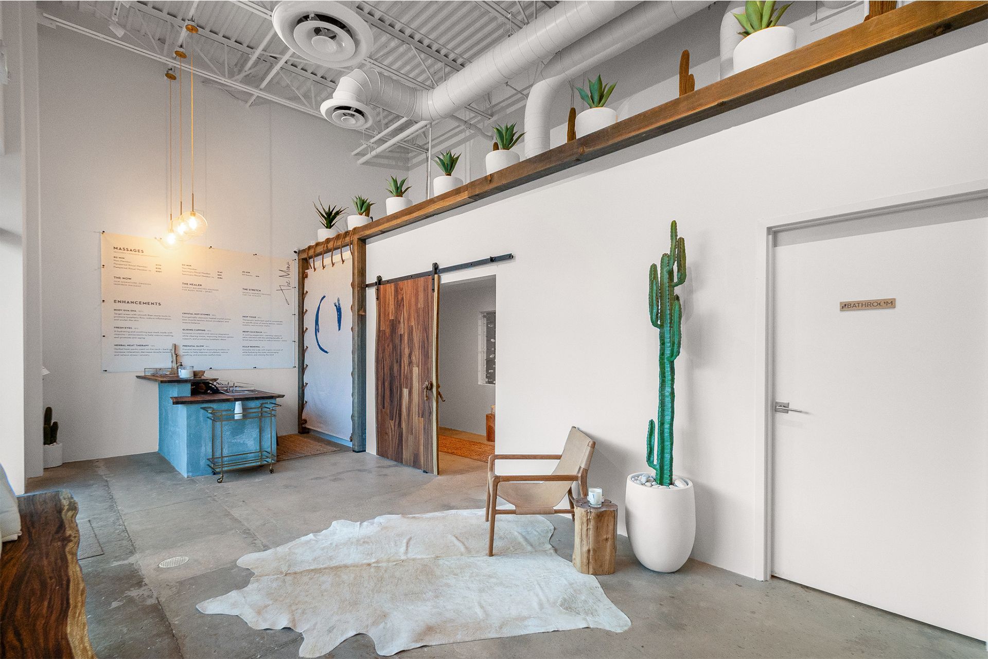Minimalist loft interior with white walls, wooden accents, cactus decor, and a blue table near the entrance