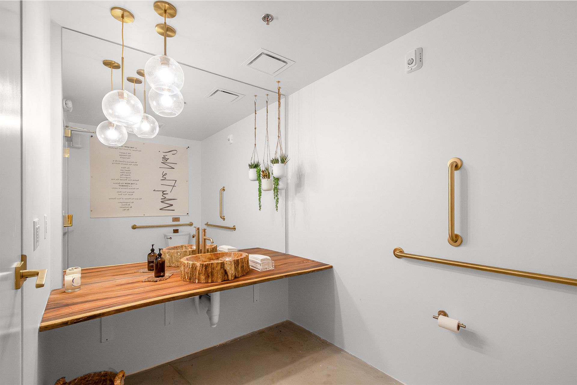 Modern bathroom with white walls, brass fixtures, floating vanity, round pendant lights, and large mirror