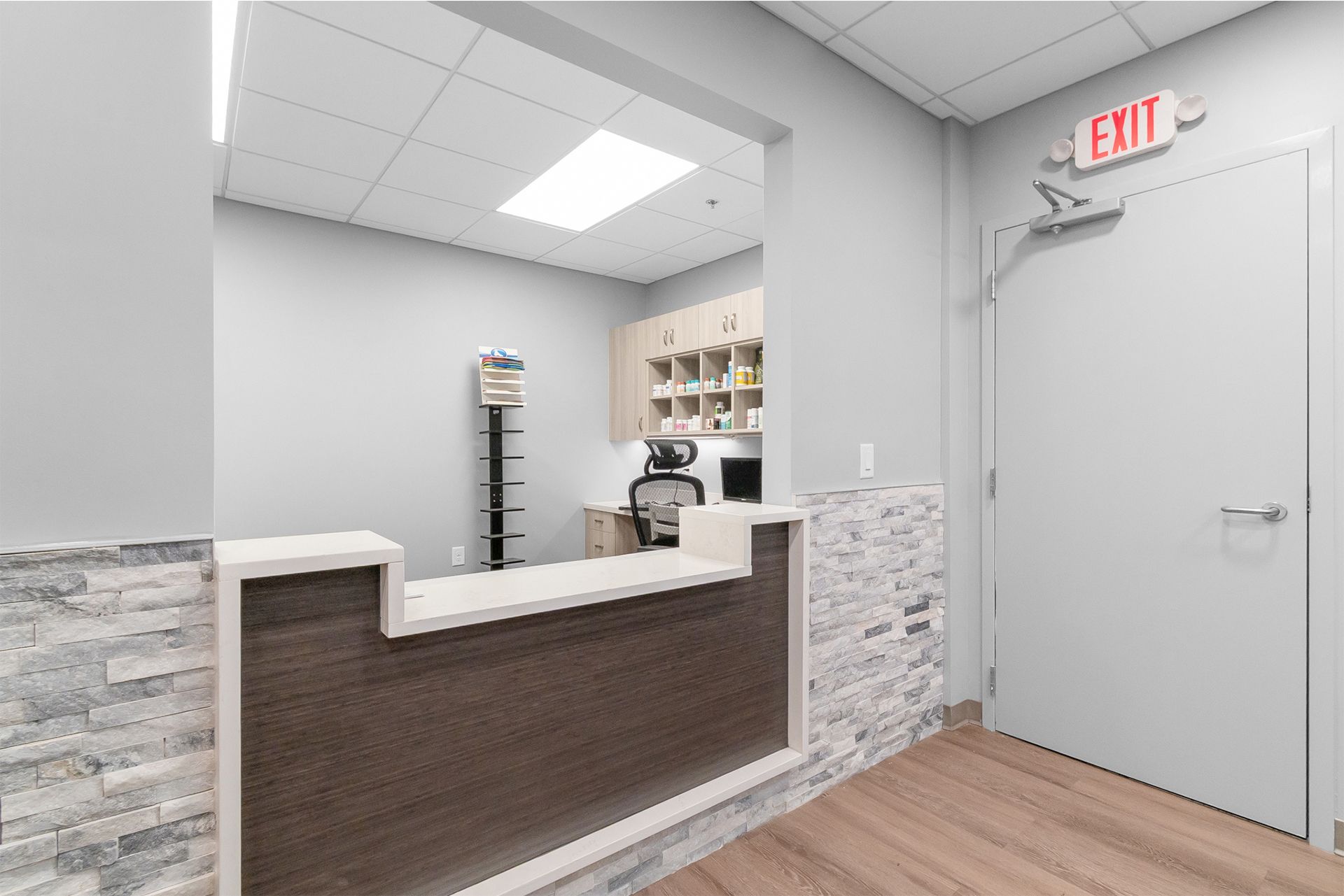 Reception area with white counter, gray walls, wood floor, and EXIT door in a clinic-like office