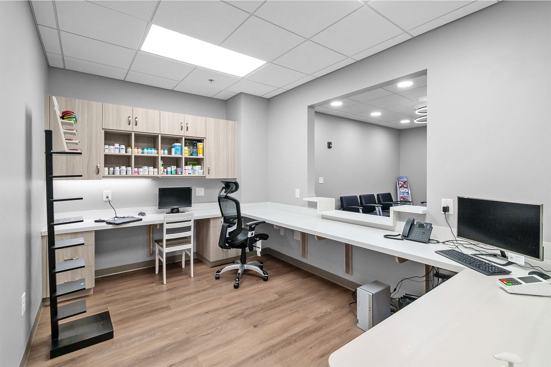 Modern office with white desks, shelves, a black chair, and computer monitors under bright ceiling lights
