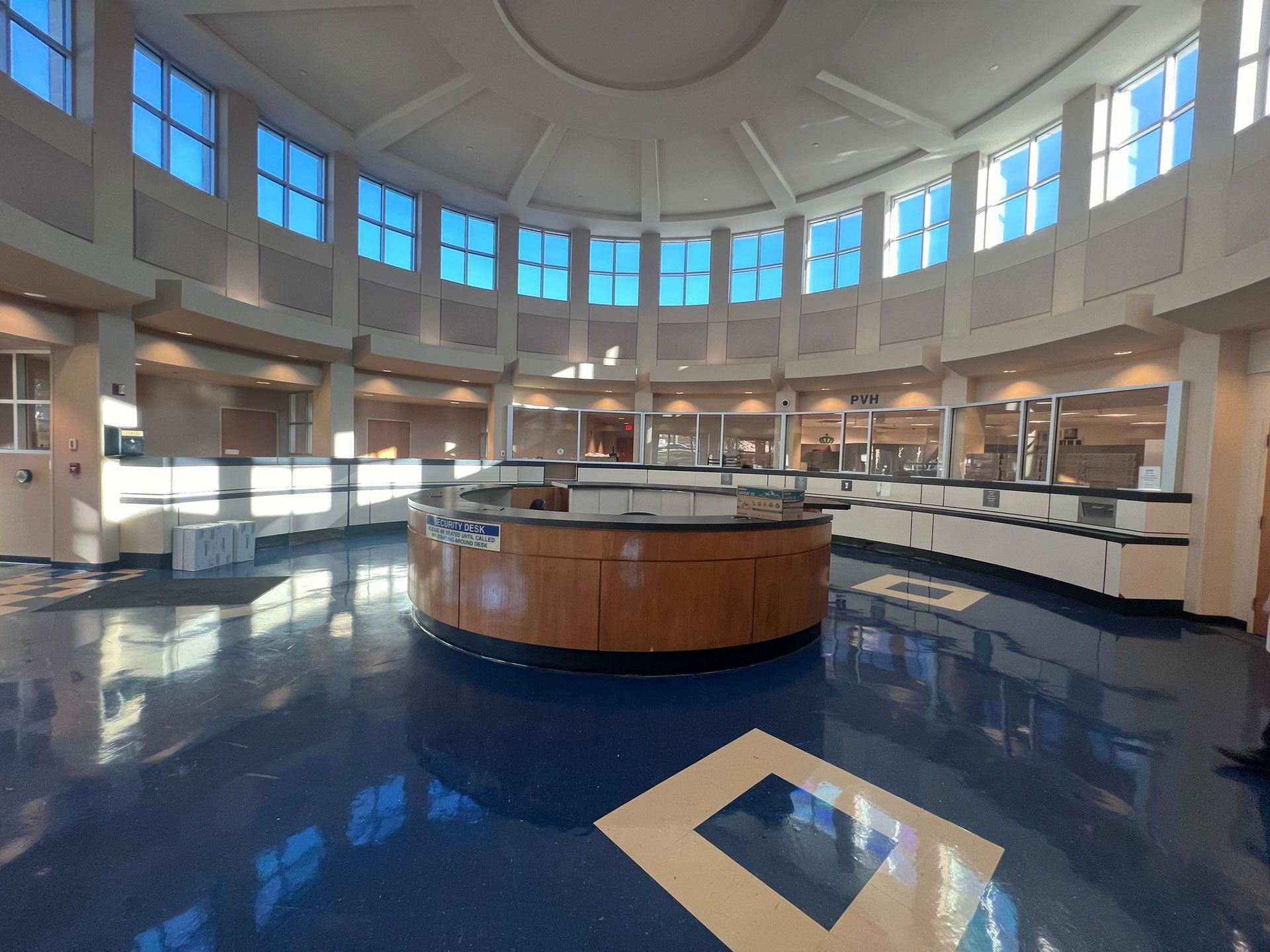 Empty circular room with a glossy blue floor and central wooden counter beneath tall windows.