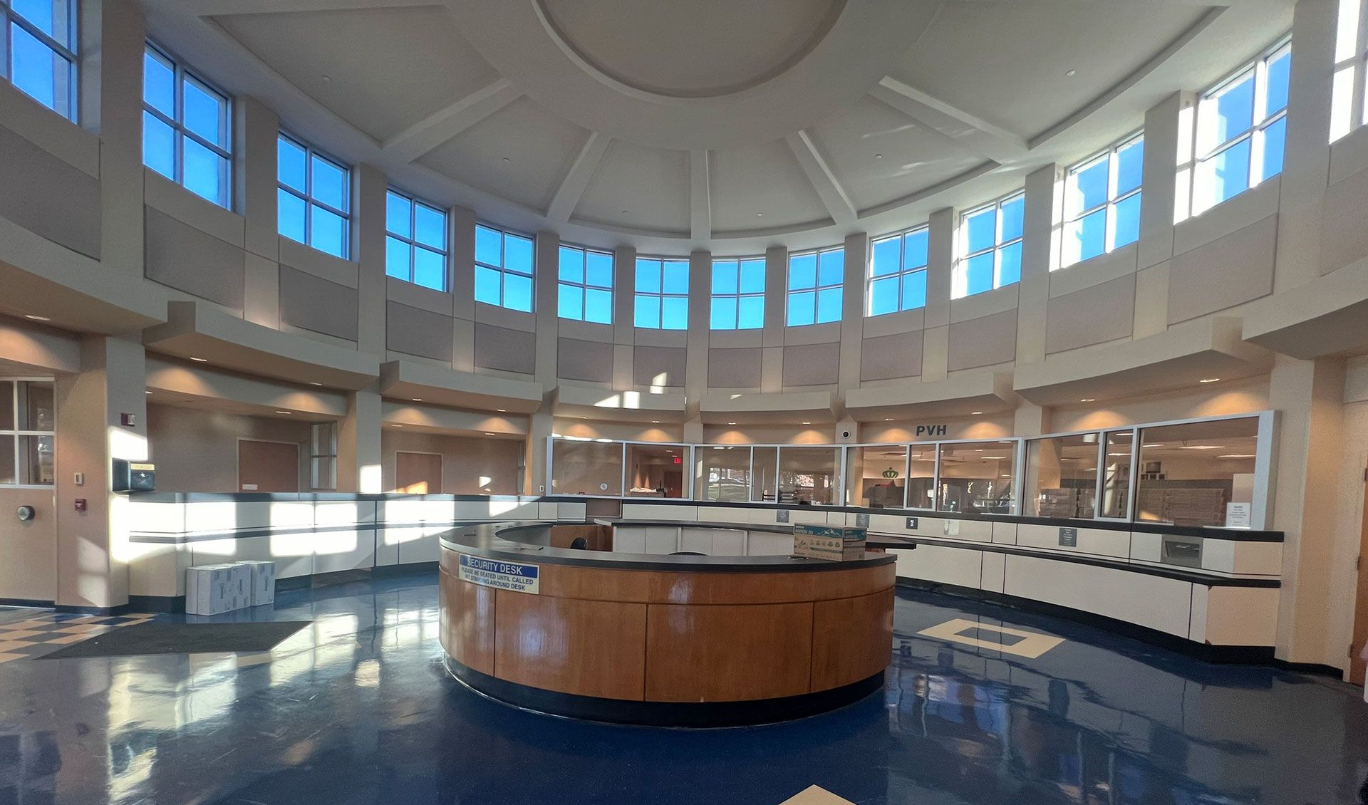 Modern waiting room with gray chairs, wood floor, white walls, and circular ceiling lights.
