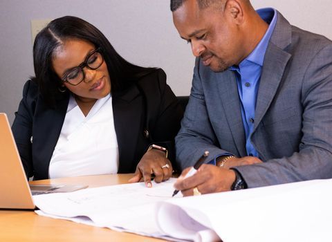 Two coworkers reviewing documents at a table with a laptop and pen in a meeting room