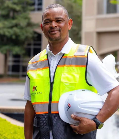 Construction worker in neon safety vest holding a white hard hat outdoors