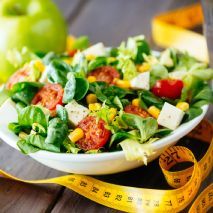 A bowl of salad next to a measuring tape on a wooden table