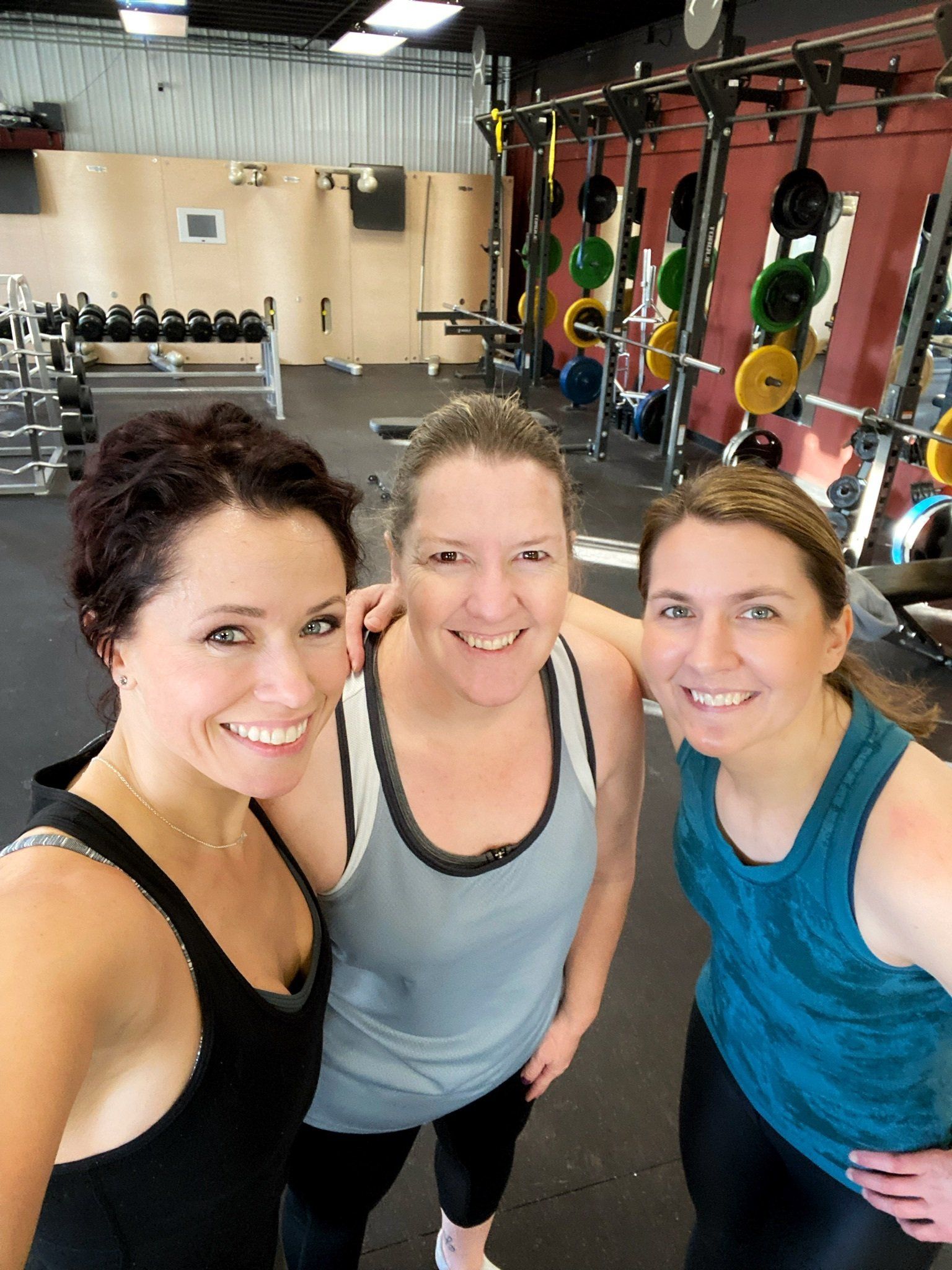 Three women are posing for a picture in a gym