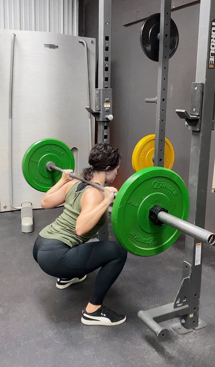 A woman is squatting with a barbell in a gym