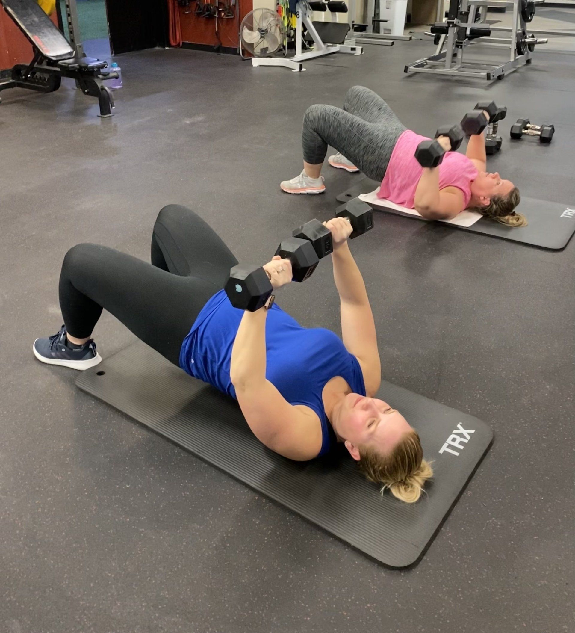 Two women are doing exercises with dumbbells in a gym