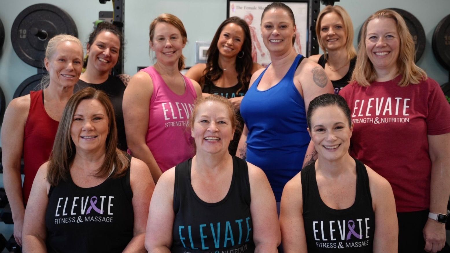 Group of women in workout attire posing in front of weights; some wearing