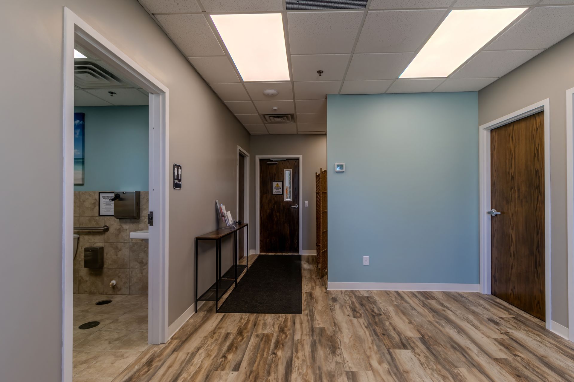 Modern office hallway with wood flooring, blue accent wall, and open doorway to a restroom.