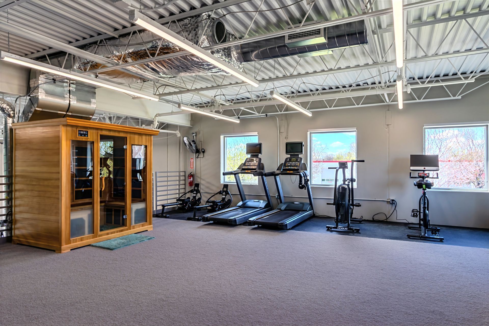 Spacious gym with treadmills, weight machines, and a wooden sauna room under exposed ceilings.