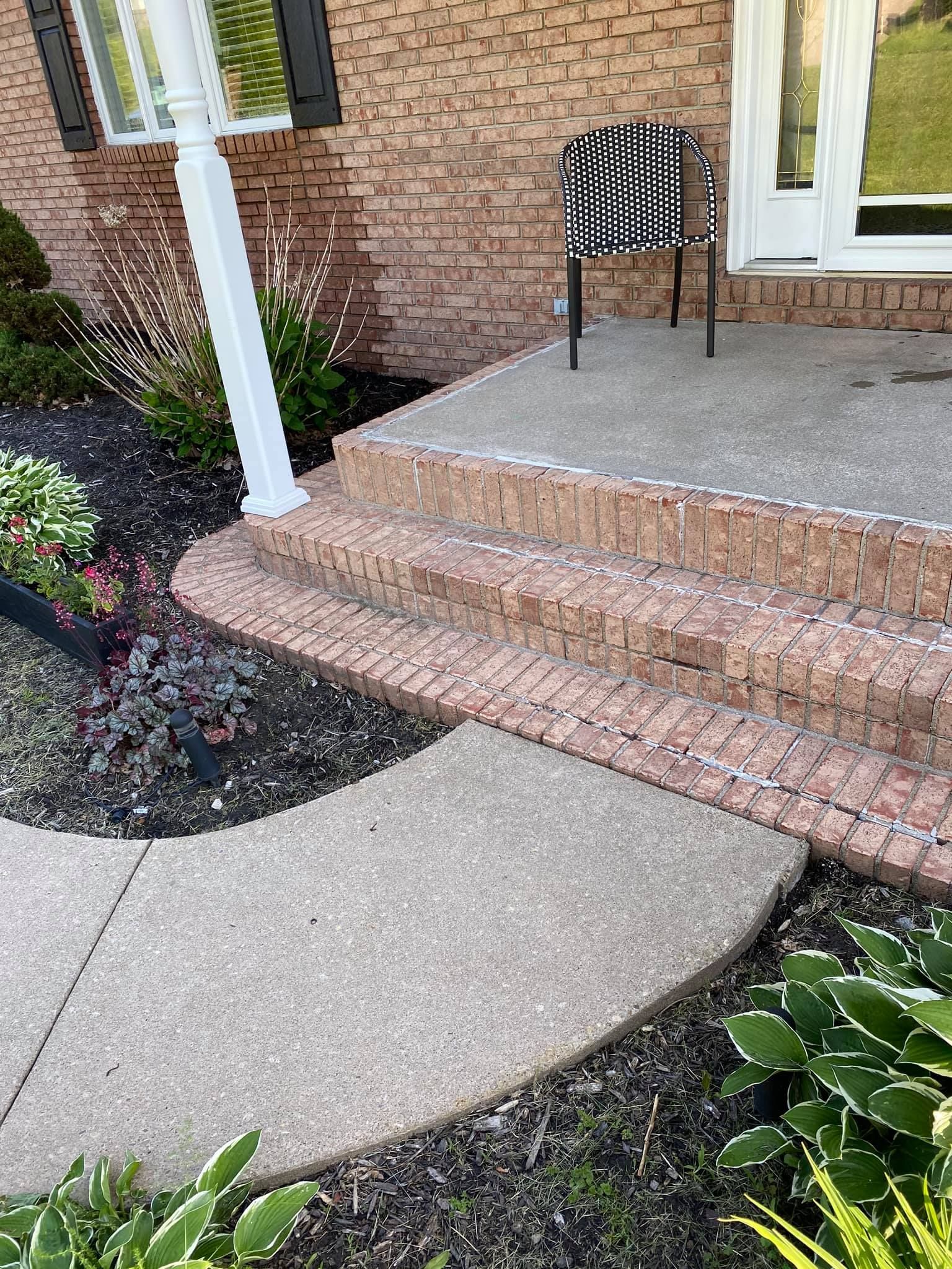 Front porch steps with brick and concrete, a striped chair on the landing, and garden beds beside the walkway
