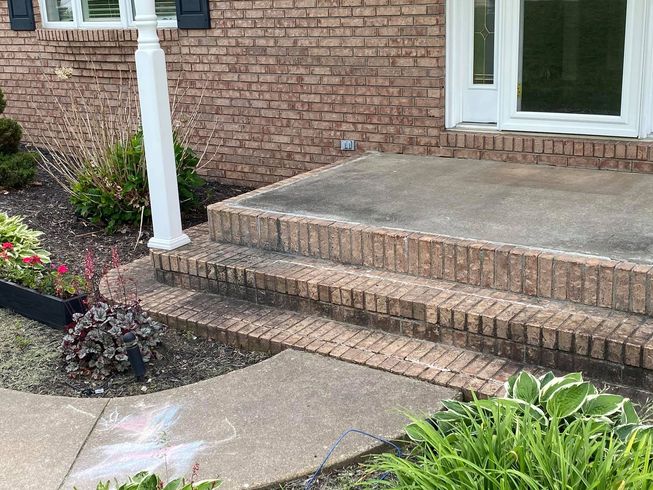 Brick house front porch with concrete steps, white column, and landscaped flower beds