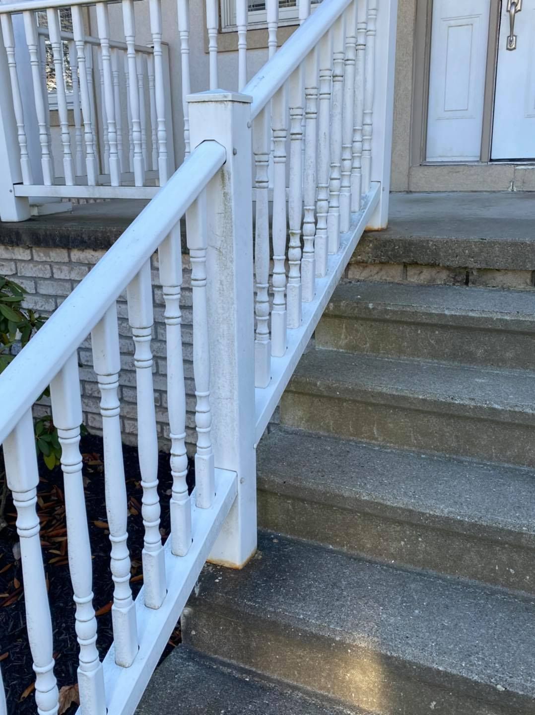 White porch railing beside gray concrete steps leading to a door