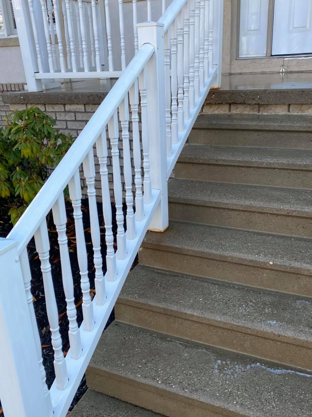White porch railing beside concrete steps leading to a house entrance.