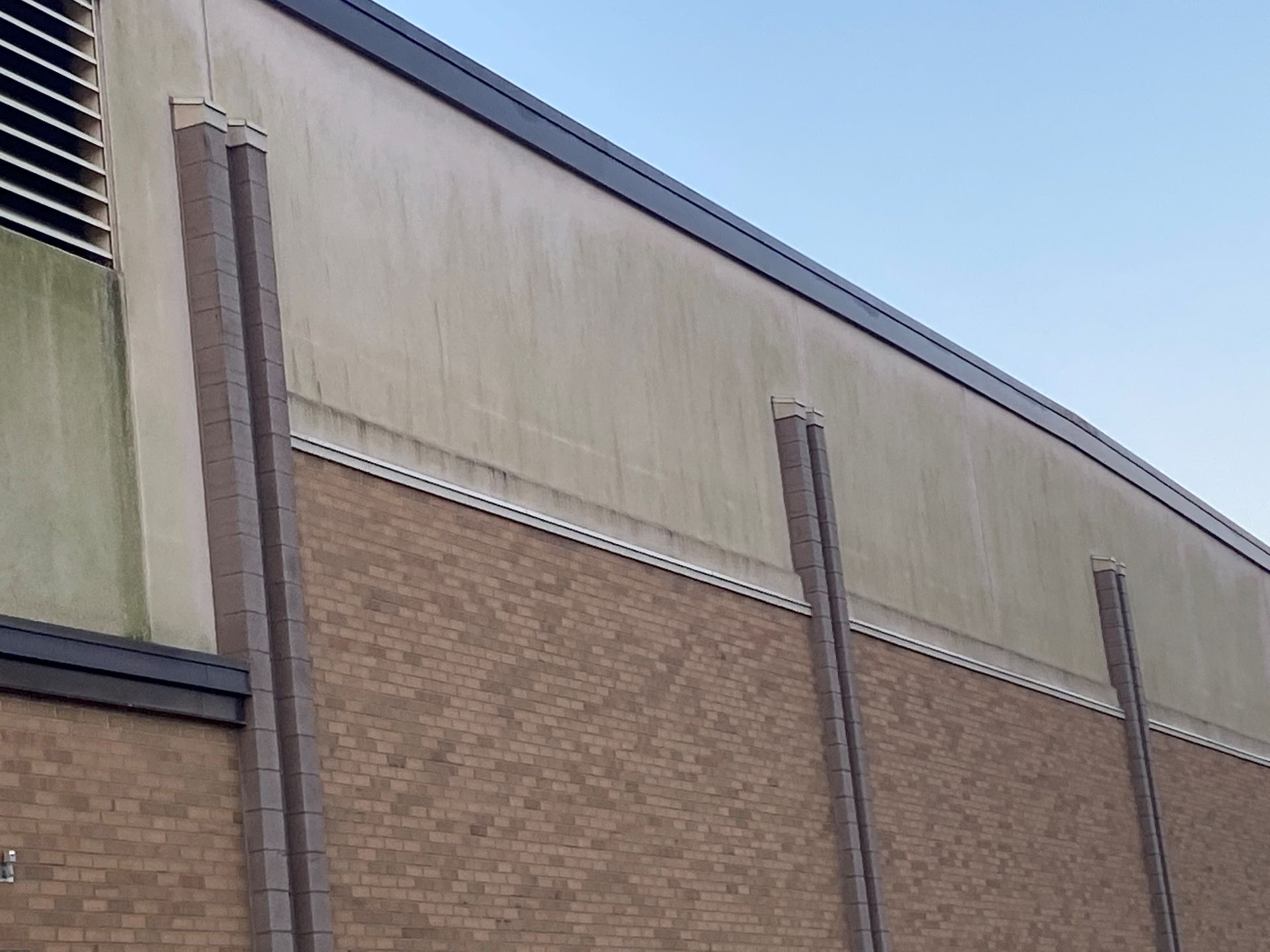 Brick building wall with tan upper facade, brown lower bricks, and vertical vents against a blue sky