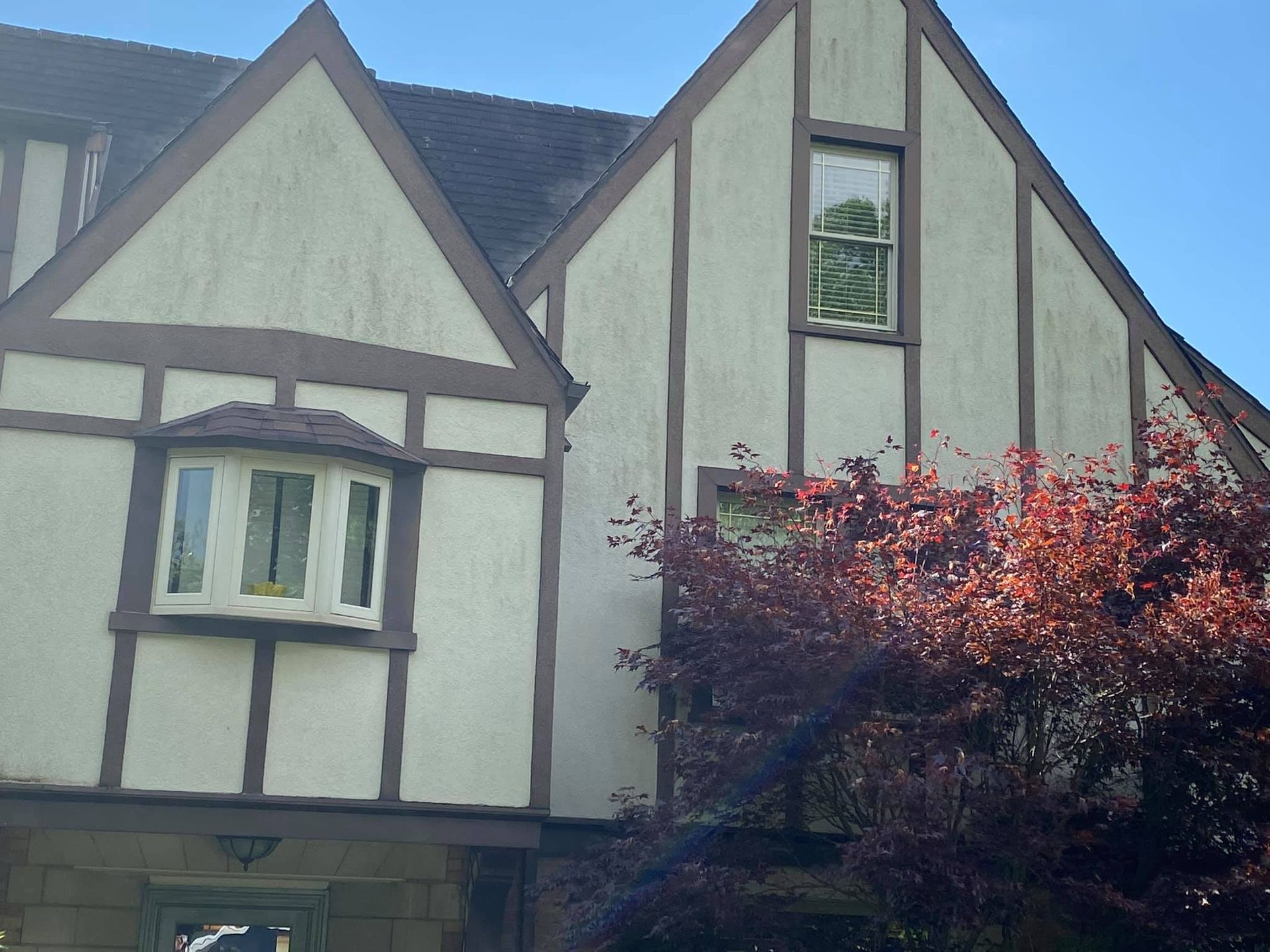 Tudor-style house with beige walls, dark trim, and a red-leafed tree in front
