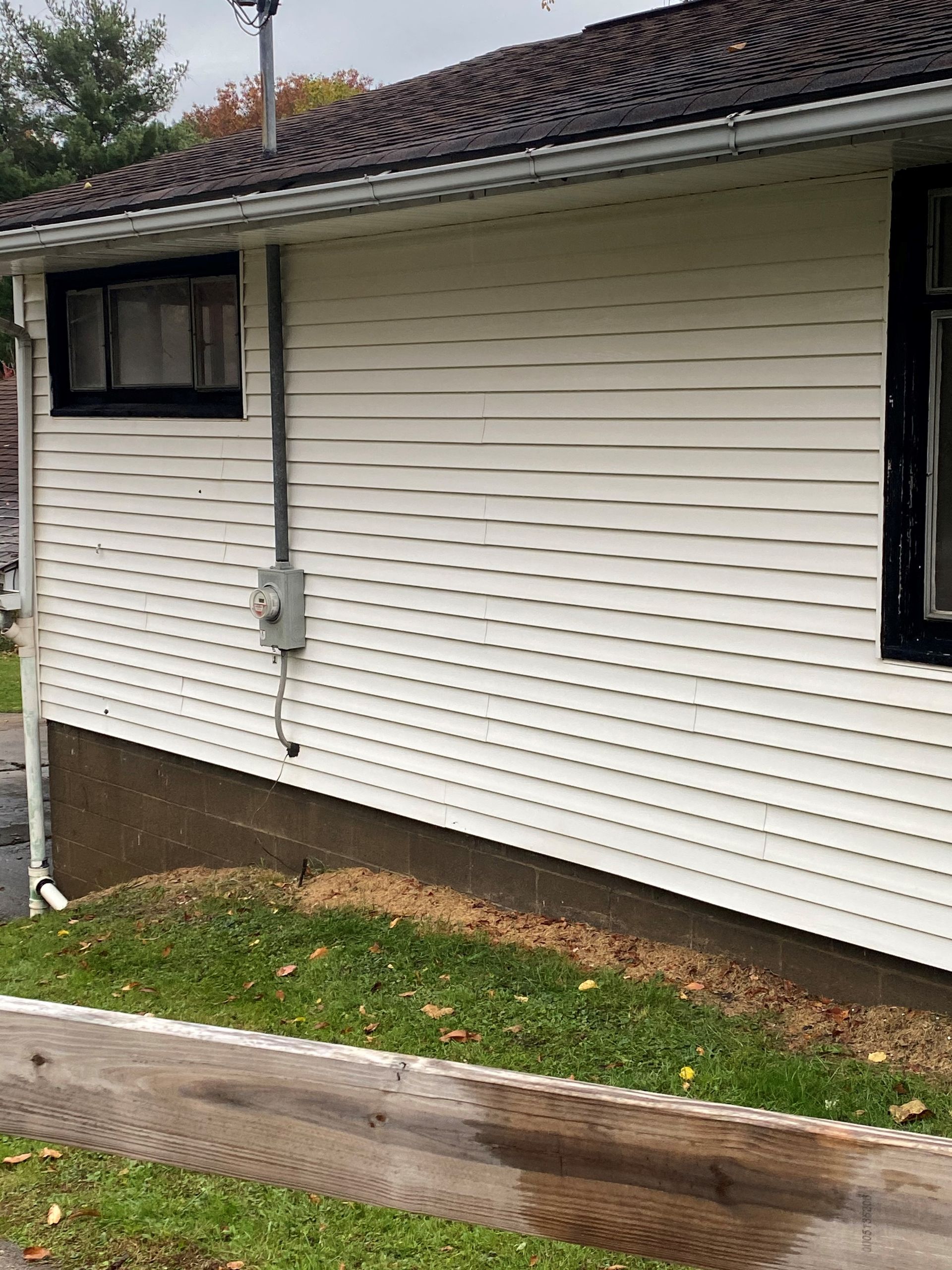 White vinyl house exterior with small window, gutter, and a narrow grass strip beside a wooden border