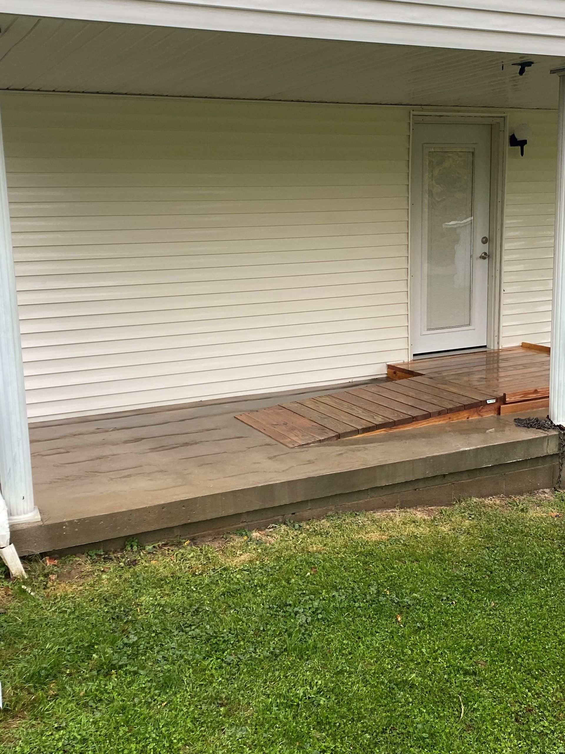 Covered porch with white siding, concrete step, and a metal ramp leading to the front door.