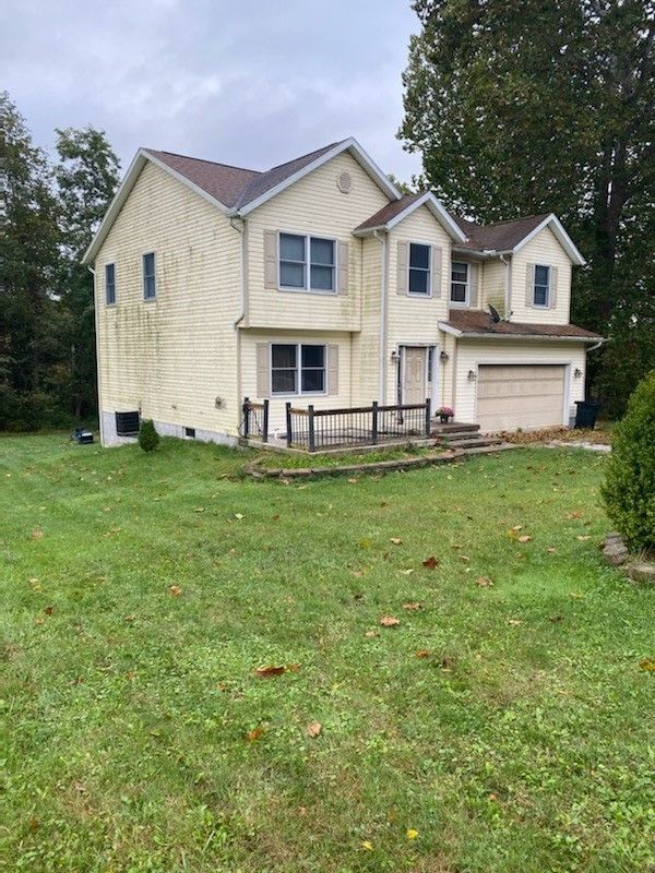 Two-story beige house with attached garage and a grassy front yard under overcast skies