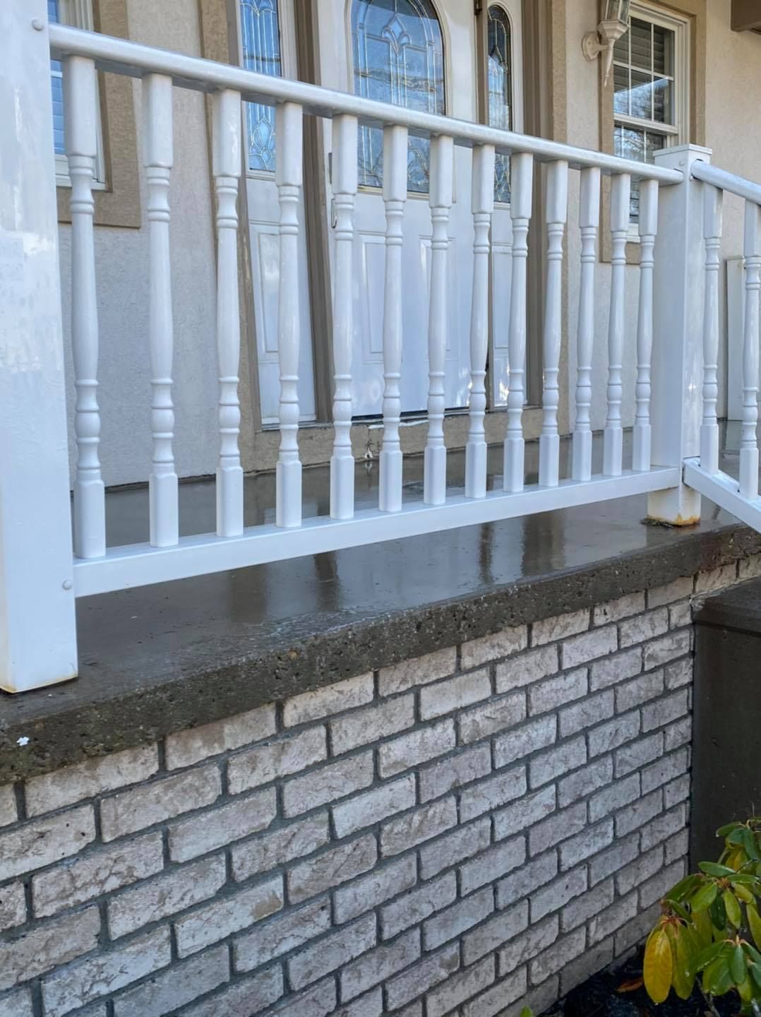 White porch railing above a gray brick retaining wall beside a house entrance