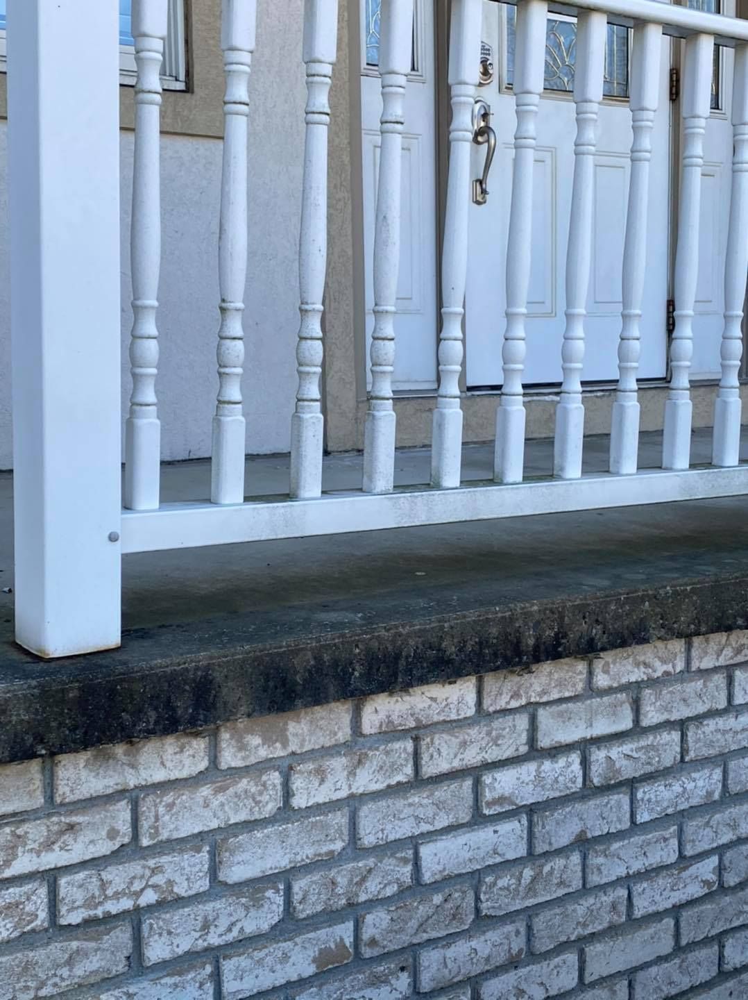 White porch railing above a gray brick retaining wall with dark water stains