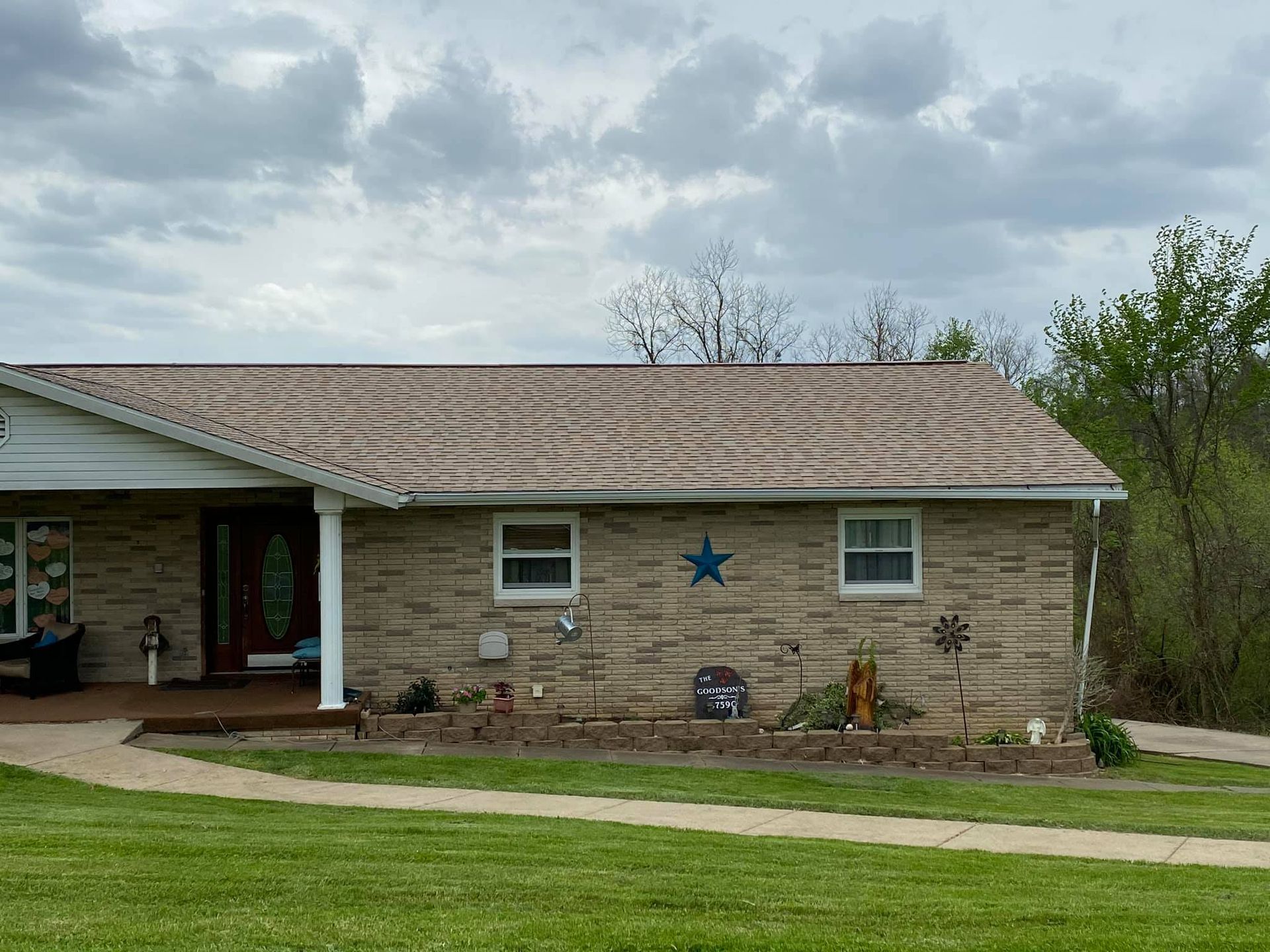 Single-story brick house with a covered porch, blue star decoration, and cloudy sky behind it