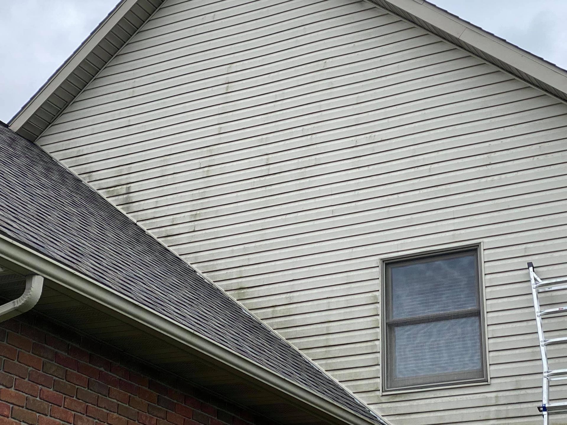 House exterior with beige siding, gray roofline, brick wall, and a small window with a ladder nearby