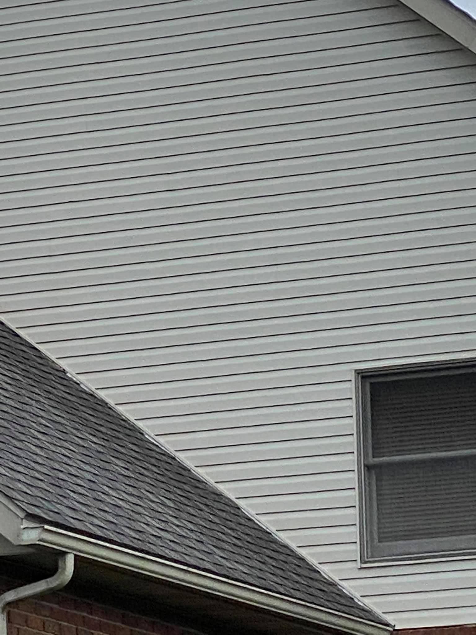 House exterior with gray siding, dark shingled roof, and a window.