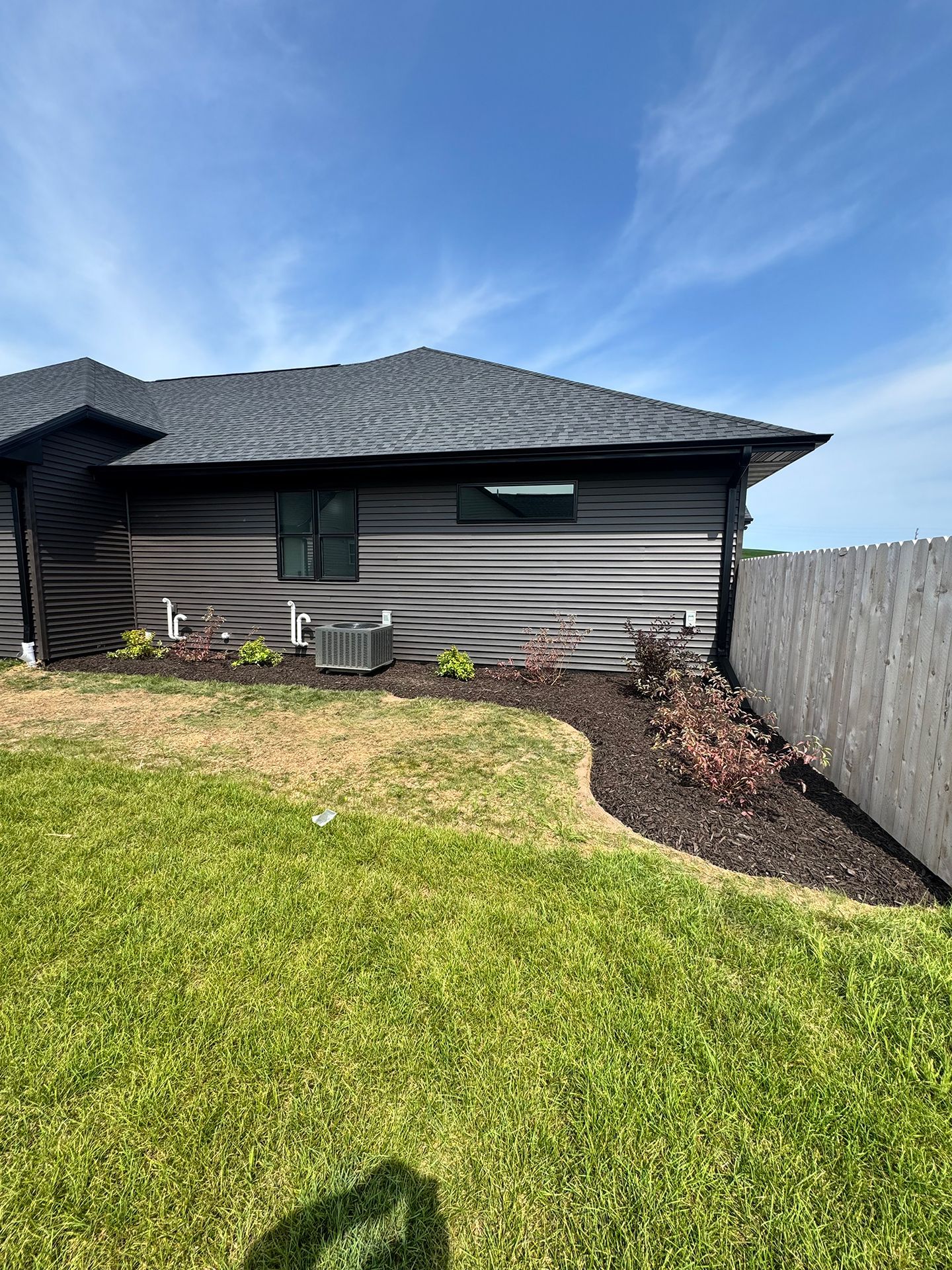 Suburban house exterior with siding, sloped roof, green lawn, and a wooden fence
