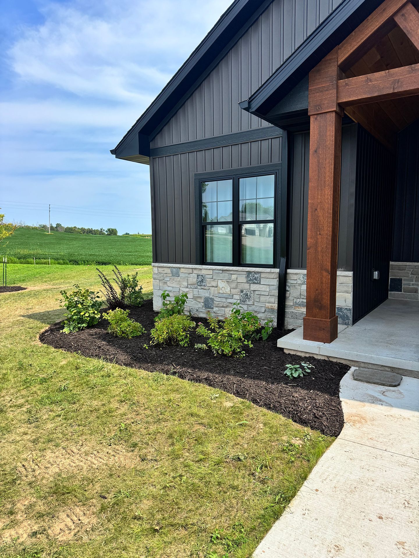 Modern farmhouse exterior with black siding, stone base, and landscaped front yard