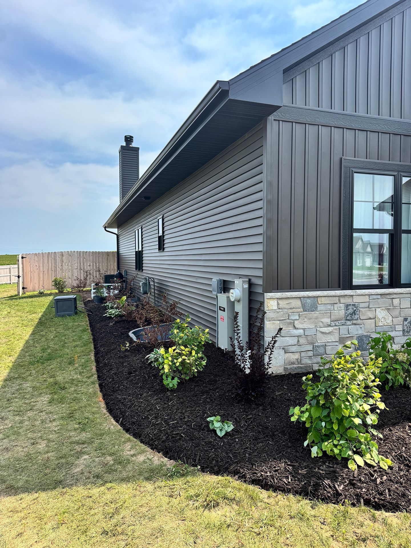Side of a house with stone base, dark mulch flower bed, and a lawn