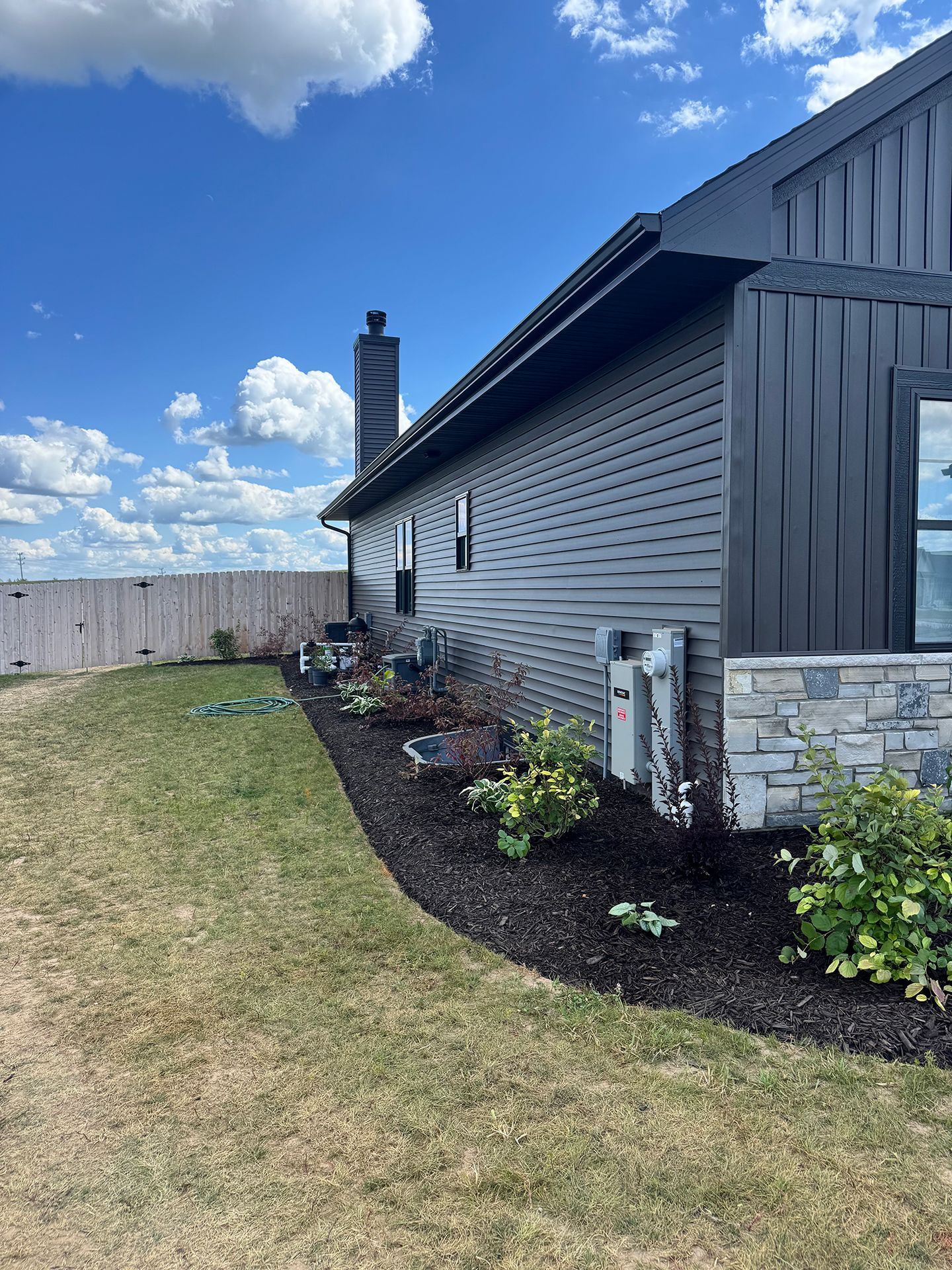 Side of a house with fresh flower beds along a lawn under a blue sky
