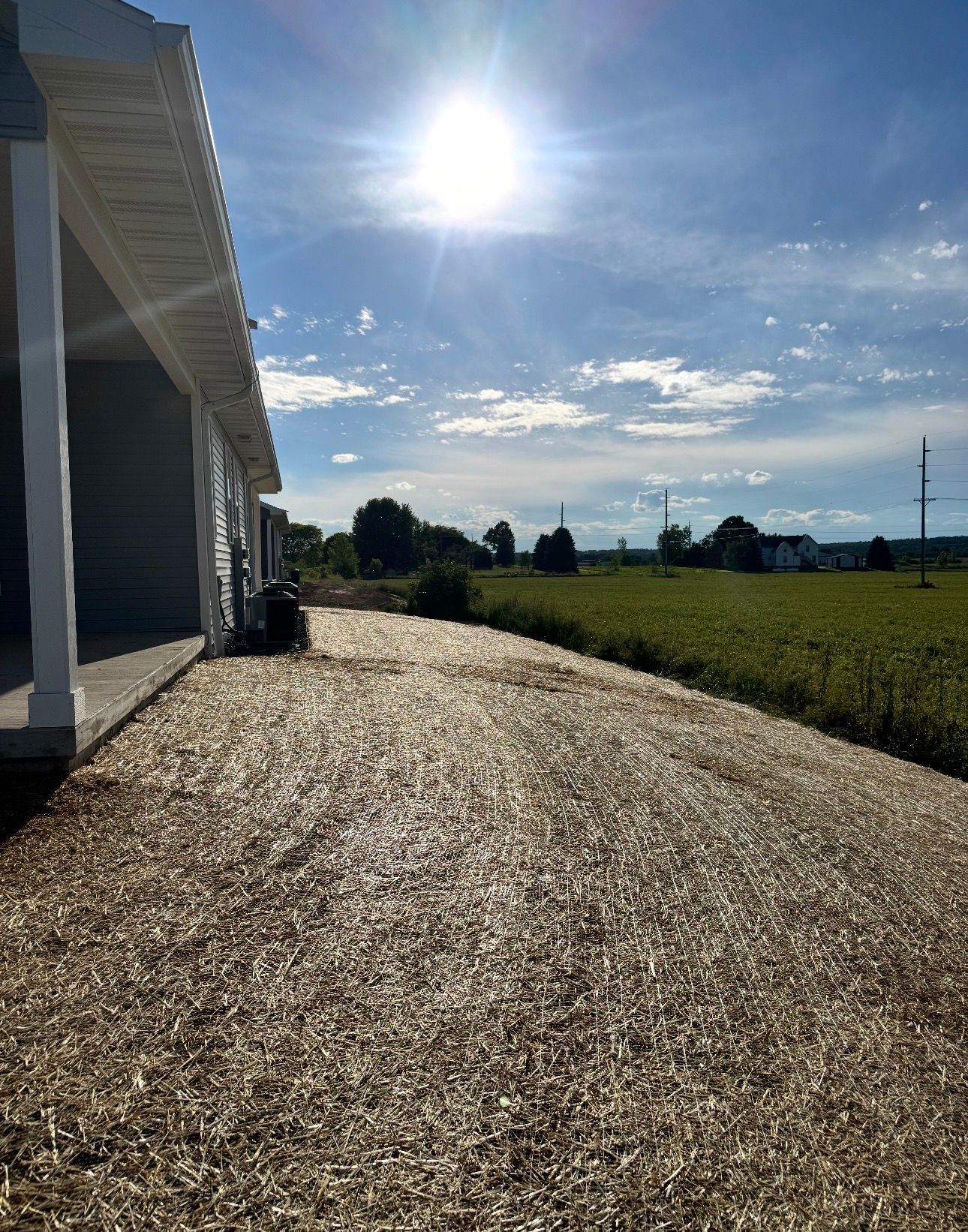 Gravel driveway beside a white house, bright sunny sky over open fields