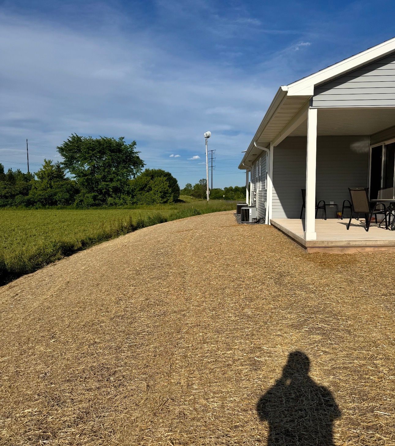 Gravel driveway beside a white house porch, with green fields and blue sky in the background.