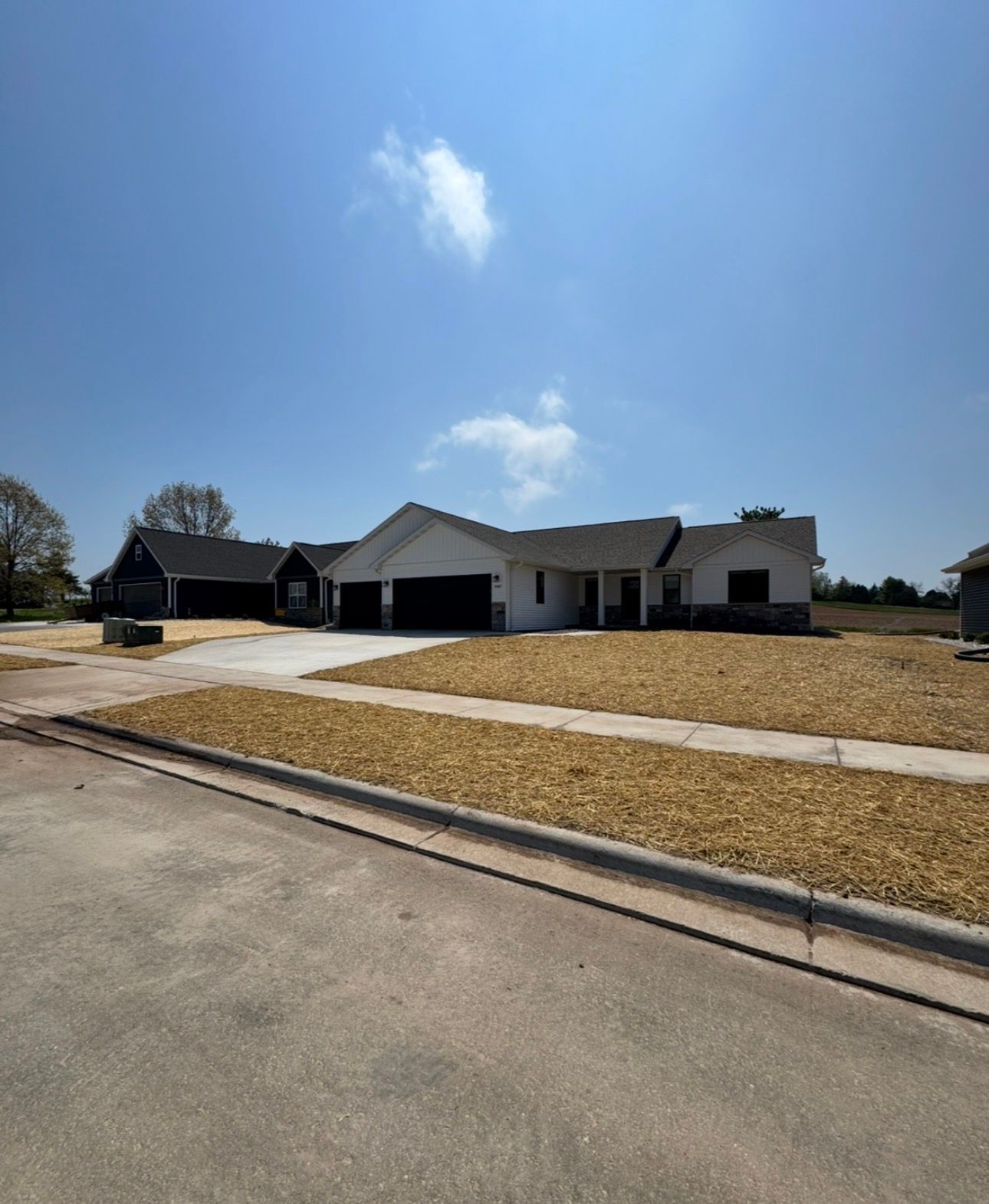 Single-story suburban house with a wide driveway, dry lawn, and bright blue sky overhead