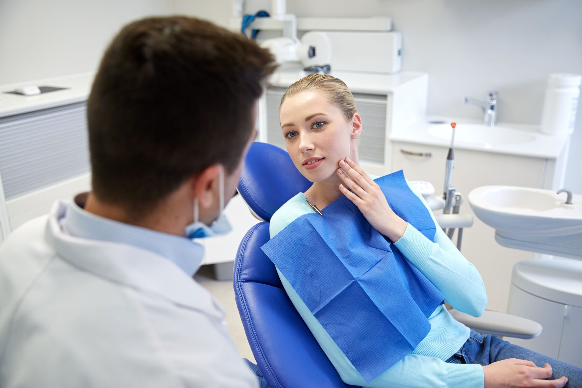 Dental patient in blue bib speaking with dentist in a bright exam room