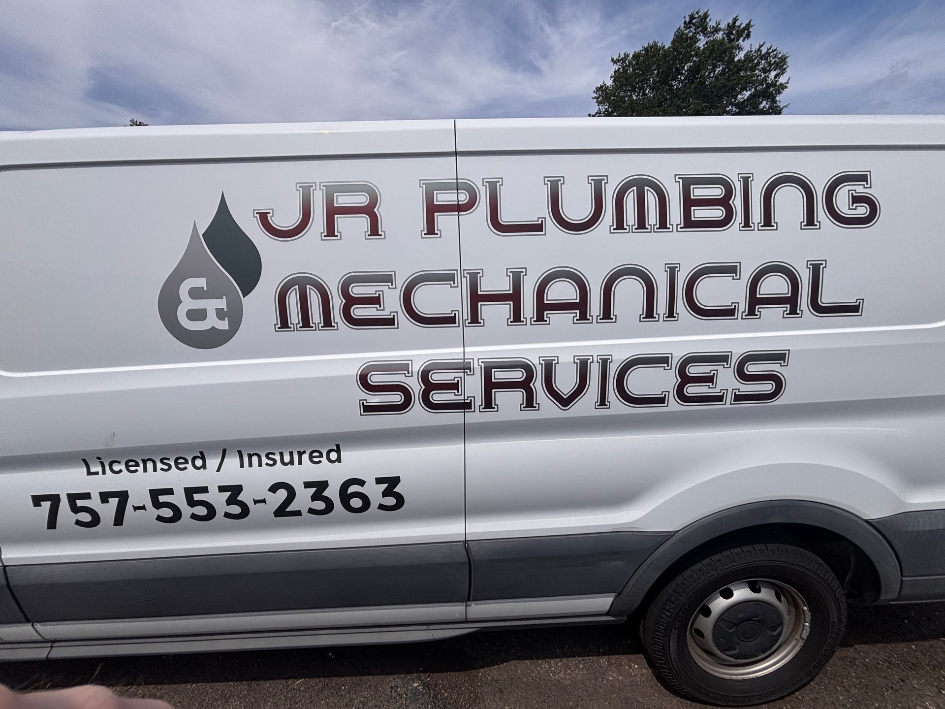 White JR Plumbing & Mechanical Services van with phone number parked outdoors under a cloudy sky